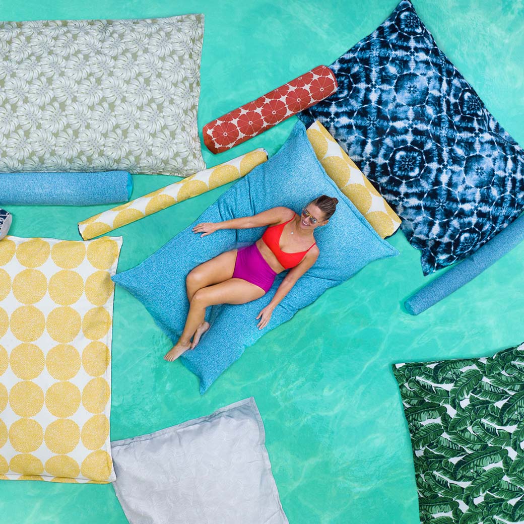 A woman lounging on a floating pool pillow, surrounded by other colorful pool floats.