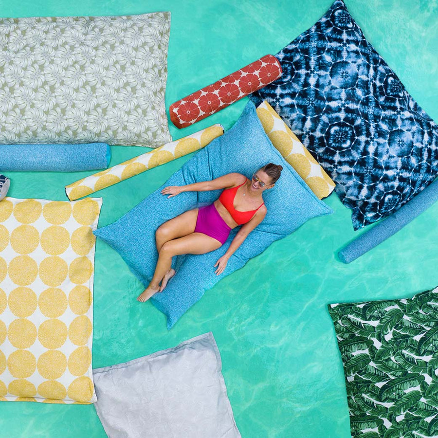 A woman lounging on a floating pool pillow, surrounded by other colorful pool floats.