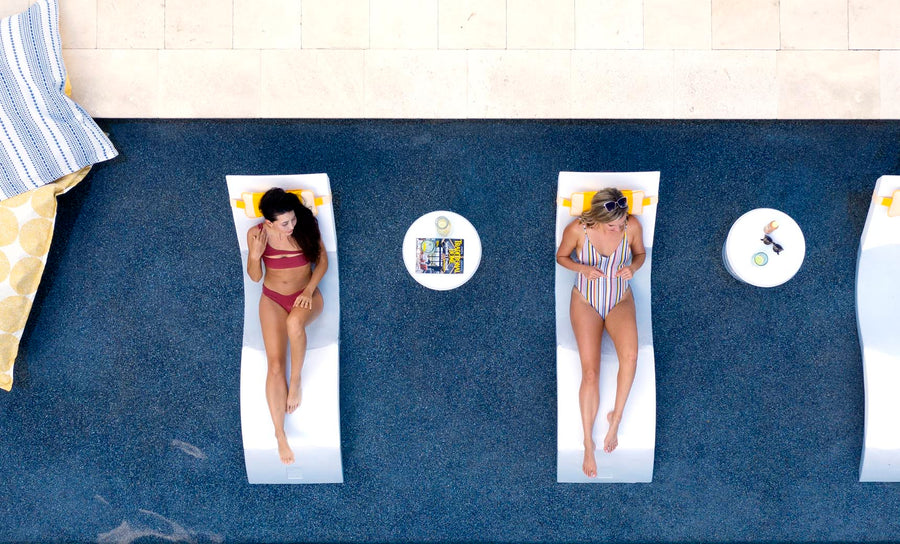 Two women lounging on in pool chaises with matching headrest pillows.