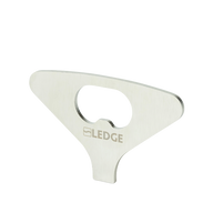 A flat, silver metal "Test Product for Transaction Test" bottle opener by Ledge Lounger, with a central opening for bottle caps and a minimalist design, stands upright against a plain white background.