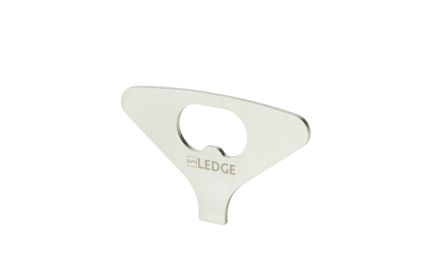 A flat, silver metal "Test Product for Transaction Test" bottle opener by Ledge Lounger, with a central opening for bottle caps and a minimalist design, stands upright against a plain white background.