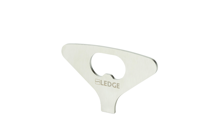 A flat, silver metal "Test Product for Transaction Test" bottle opener by Ledge Lounger, with a central opening for bottle caps and a minimalist design, stands upright against a plain white background.