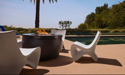 Outdoor setting with a fire pit, chairs, and a pool under a clear blue sky.