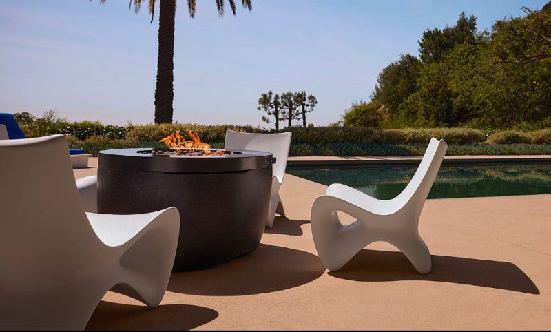 Outdoor setting with a fire pit, chairs, and a pool under a clear blue sky.